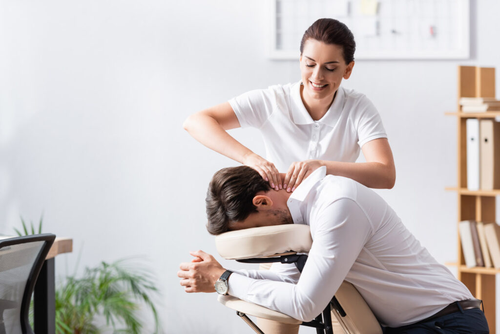 Happy masseuse doing neck massage for businessman in office on b